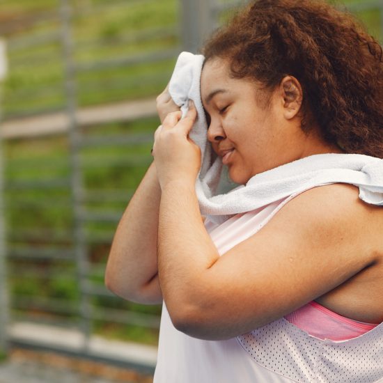 Young tired plus size woman. Girl training in a park. Woman wipes his face with a towel.